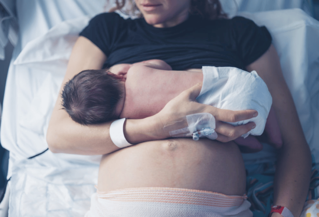A mum feeds her newborn baby in a hospital bed - Anya baby & breastfeeding app by LatchAid