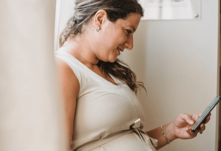 A pregnant expectant mum checks her phone - Anya baby & breastfeeding app