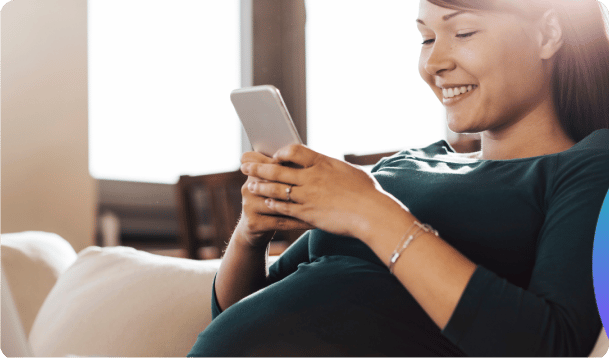 A smiling pregnant woman checks on her phone - Anya baby & breastfeeding